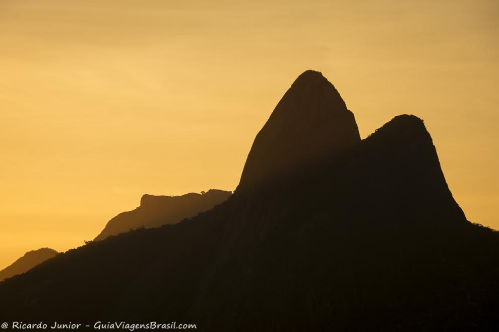 Imagem de dois morros com o céu alaranjado.